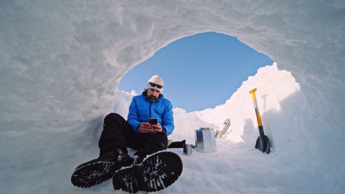 成熟的游客在雪地里用手机喝咖啡。在大自然中独自在冬天的山上露营。