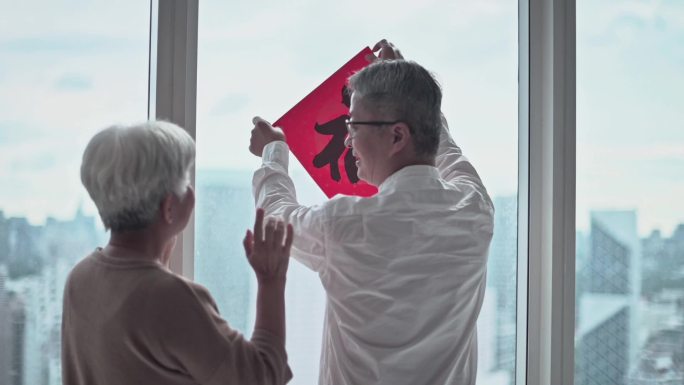 中国新年高级夫妇在窗户上用中国书法装饰房子客厅，为家庭团聚做准备