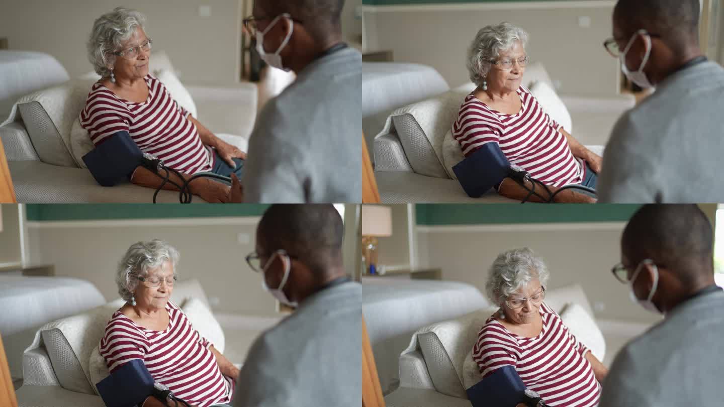 医生在卧室里测量一位老年女性的血压——戴着口罩