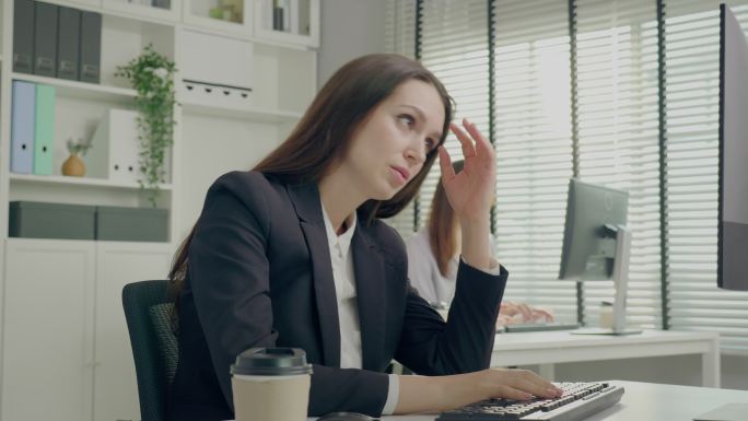 美丽的年轻女商人在工作失误后倍感压力，年轻的亚洲女性坐在办公桌前，手里拿着电脑