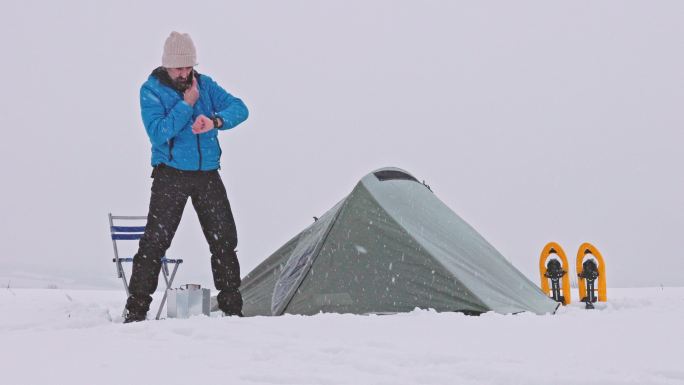 成熟的游客在大自然中独自在冬天的山上露营时使用电话。