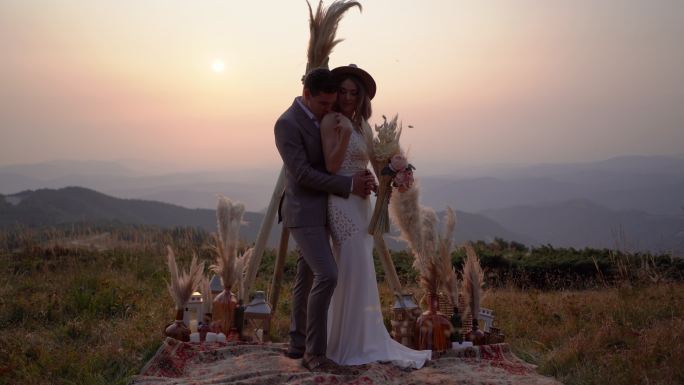 日落时分，幸福的新婚夫妇站在山上拥抱