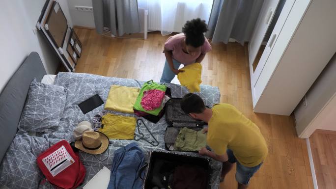 不同种族的情侣为度假打包行李箱-两人度假打包衣服的高视角