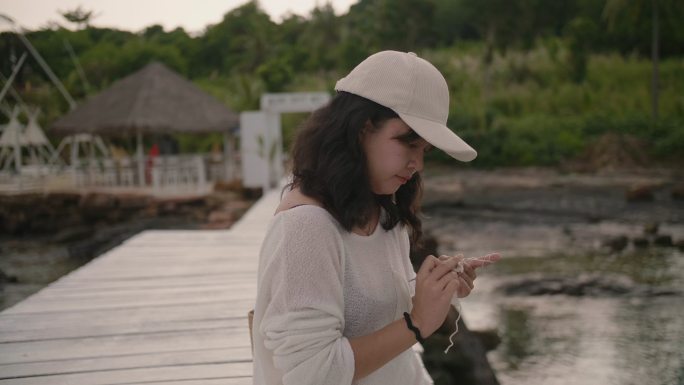 年轻女子坐在通往大海的木制码头上的侧视照片和休闲时间钩针编织