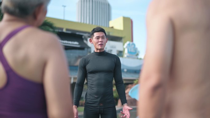 亚洲中国男游泳教练在池边游泳课前向他的高年级学生解释
