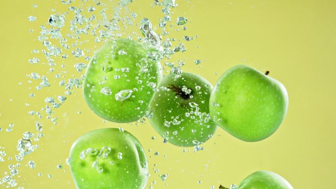 苹果在橄榄绿的背景下缓慢地落入清澈的水中。新鲜、多汁、美味的苹果掉进水中产生气泡的特写镜头。保持健康