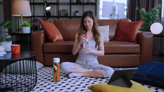 有吸引力的年轻亚洲青少年女性在家健身后喝一瓶清爽的饮料健康和思想理念，在家锻炼