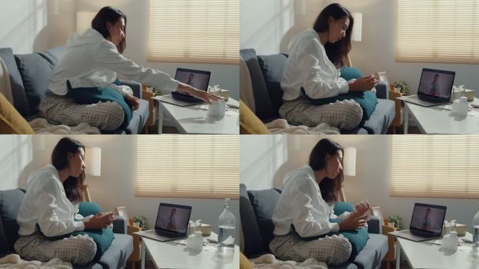 生病的年轻亚洲妇女在家里的客厅里用笔记本电脑和坐在沙发上的医生交谈。