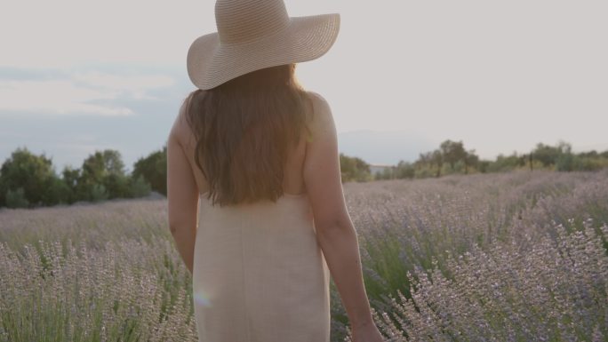 日落时分，身着夏装、头戴遮阳帽的年轻女子在薰衣草地里穿行