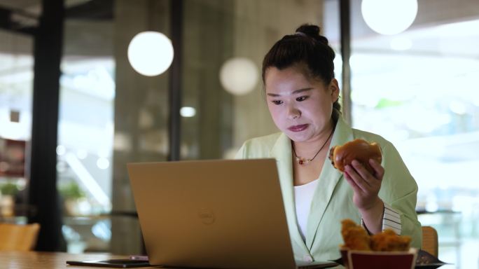 身材魁梧的女性在餐厅里紧张地吃汉堡包和使用笔记本电脑