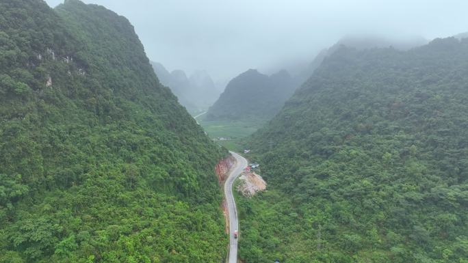 无人机在雾蒙蒙的蜿蜒山路上飞行，靠近雾蒙蒙的雨林树木。电影镜头鸟瞰雄伟的热带山脉景观。越南北部