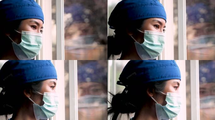 过度劳累、担忧、忧郁、压力重重的亚洲女性医护人员透过窗户看