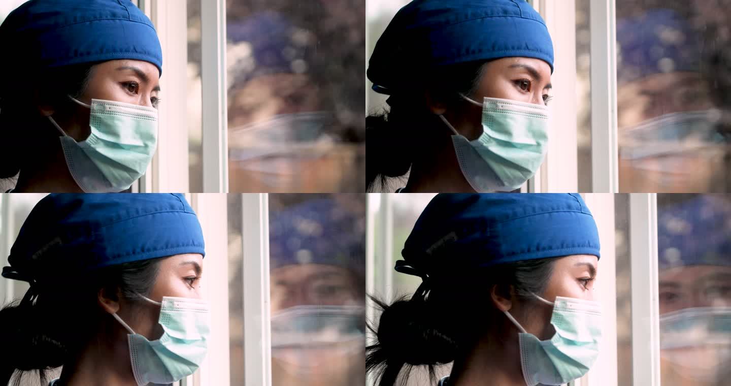 过度劳累、担忧、忧郁、压力重重的亚洲女性医护人员透过窗户看