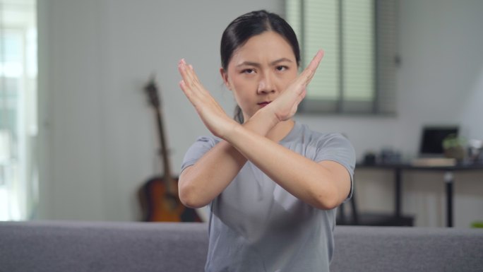 一名亚洲妇女坐在家里的沙发上，愤怒地双臂交叉。