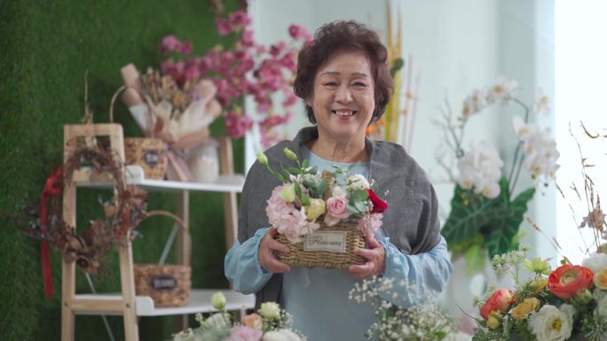 在插花课结束后，骄傲的亚洲中国高级女性拿着自己的花篮在花店里微笑着看着镜头