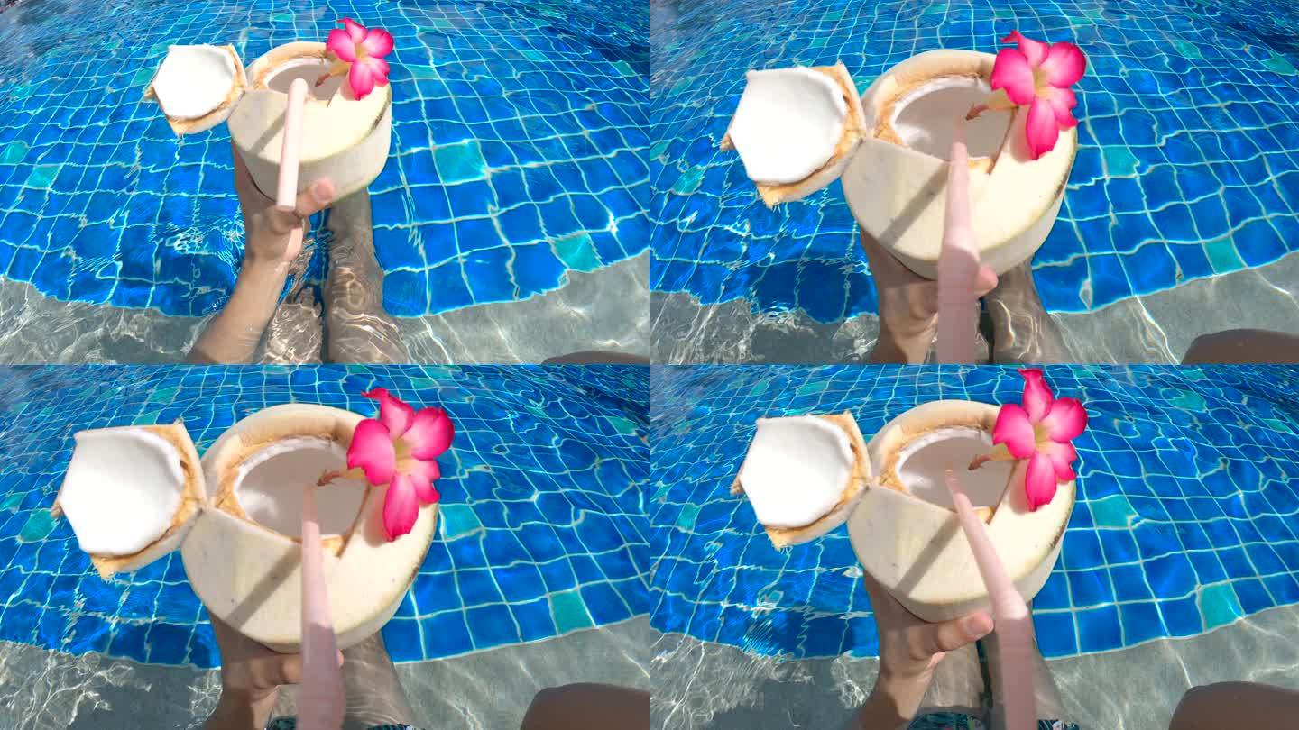 POV个人视角男人在阳光明媚的热带游泳池喝椰子饮料