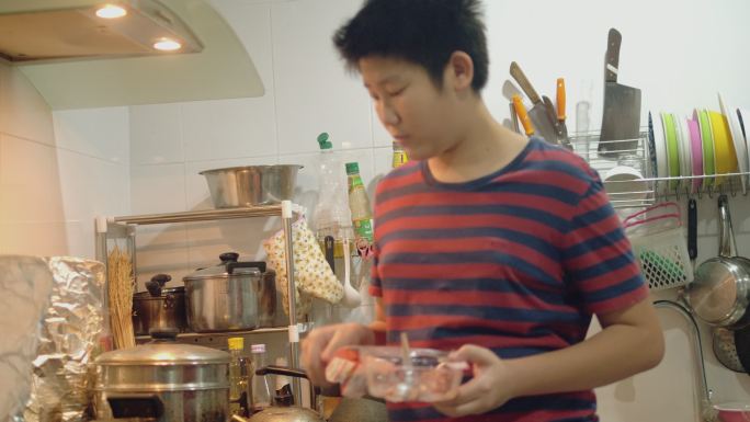 亚洲男孩在家里的厨房里用炉灶做饭，周末生活方式理念。