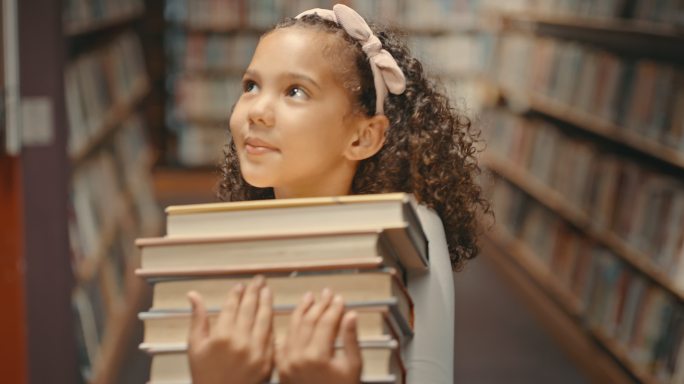 小女孩独自在图书馆里。做研究的幼童。可爱的孩子在图书馆做学校作业。