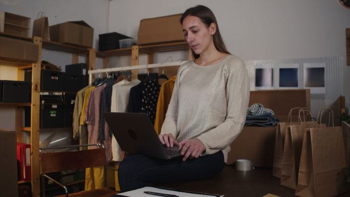 一名年轻女子正在她的新网上服装店检查她的笔记本电脑