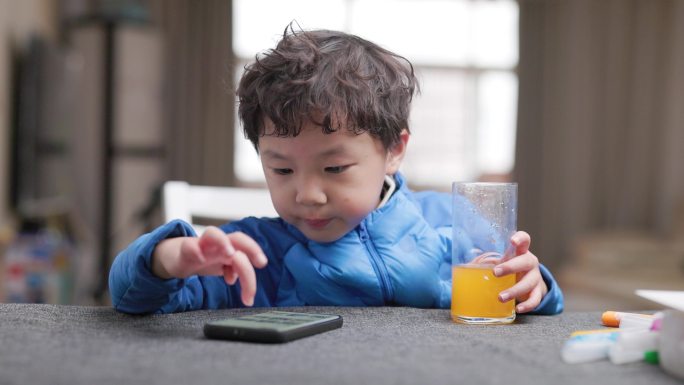 小男孩一边喝橙汁一边玩手机