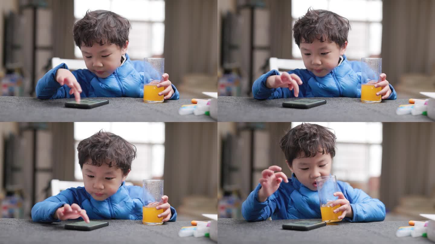 小男孩一边喝橙汁一边玩手机