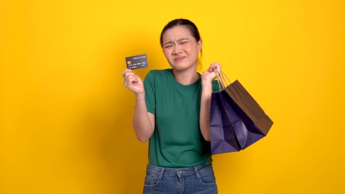 一名亚洲女性因持有更多购物袋和信用卡而感到焦虑，并被隔离在背景之外。