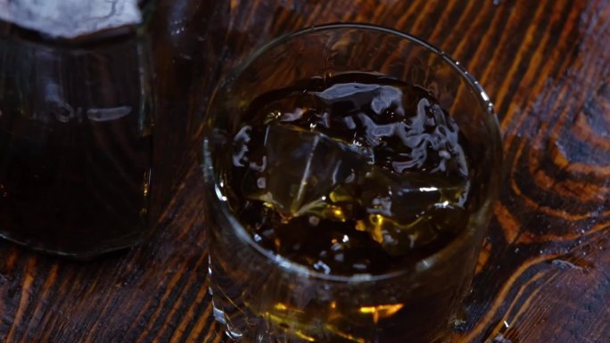 冰块掉进了棕色木头上的威士忌杯中