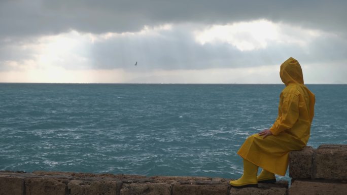 穿着黄色雨衣的年轻人望着海边的大海，看鸟