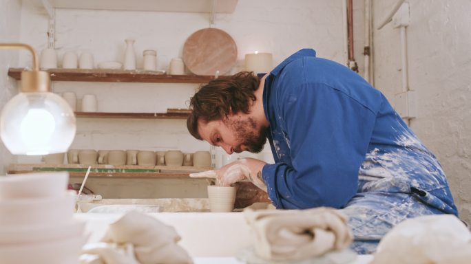 在一个陶瓷艺术工作室里，年轻的陶艺家用手在陶轮上制作一个泥杯。艺术创意陶工造型，在业余手工作坊中用天