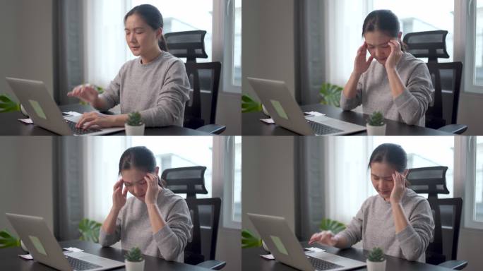 一名亚洲妇女在家办公时用笔记本电脑工作，头痛得很厉害。