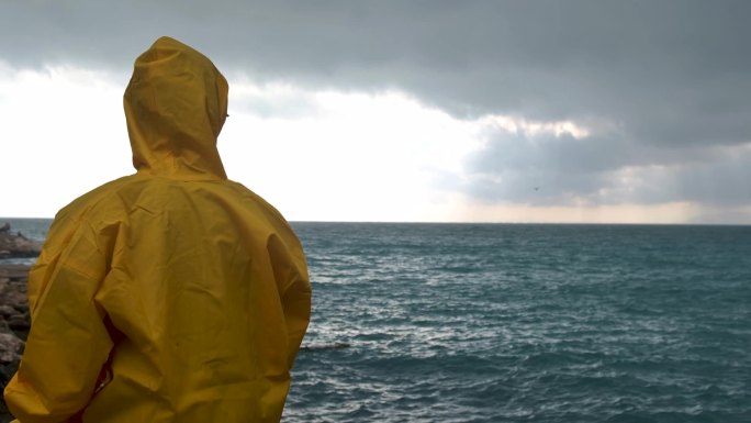 穿着黄色雨衣的年轻人望着海边的大海，看鸟