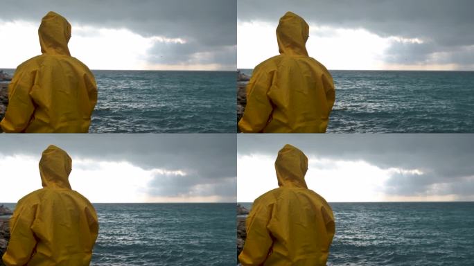 穿着黄色雨衣的年轻人望着海边的大海，看鸟