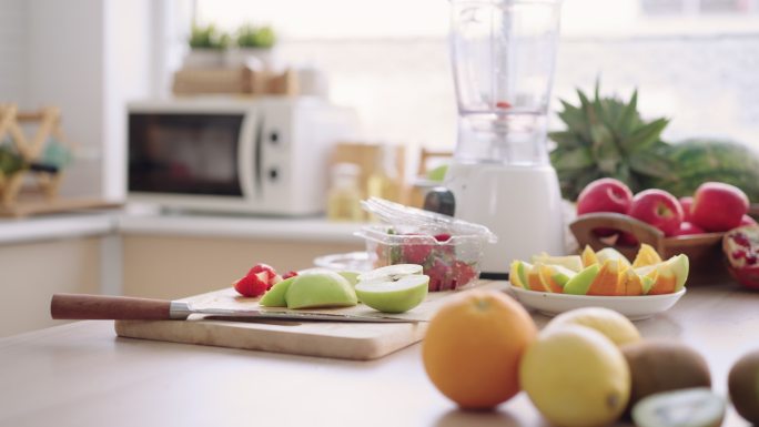 早上在家庭厨房用电动搅拌机制作草莓、苹果、橙子和石榴自制冰沙的入口，低角度侧视图