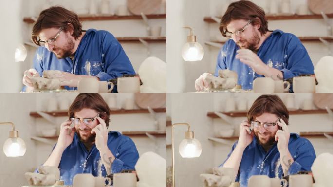 压力很大的陶艺家在陶艺工作室雕刻粘土，头疼不已。艺术创意陶艺家用手揉额头，挣扎着，充满压力。工作过度
