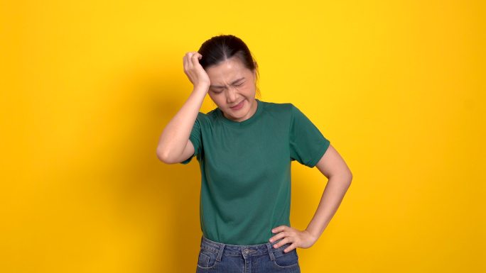 一名亚洲妇女因头痛而生病，站在黄色背景下。