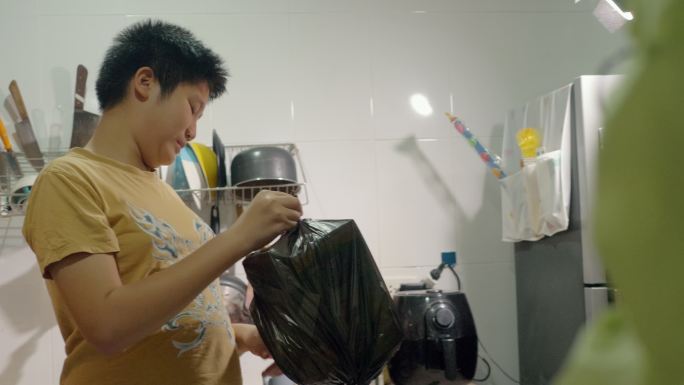 亚洲男孩在厨房里绑起黑色垃圾袋，然后扔到户外垃圾桶里，这是一种生活方式。