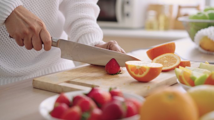 准备用草莓、苹果、橙子和石榴自制冰沙，用高级女性的手将水果切成小块，低角度侧视图