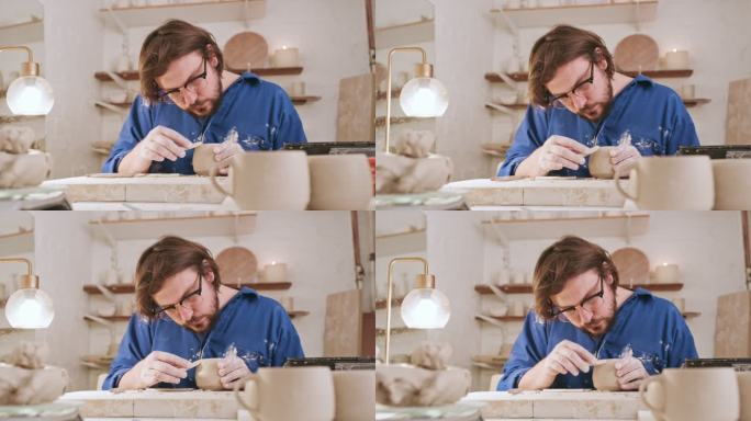 男雕塑家在他的陶器作坊里用工具雕刻一个陶罐。陶瓷艺术家、陶艺家或手工艺人，制作手工杯子或碗，为自己的
