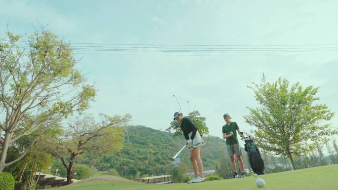 亚洲年轻女子高尔夫球手在高尔夫练习场教年轻人打高尔夫