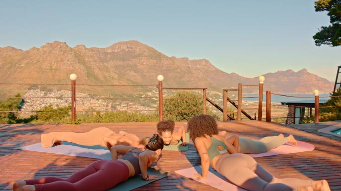 一群年轻女性在日落时只做瑜伽俯卧撑，欣赏风景和文案。适合朋友在一个和平的度假胜地，在健身垫上，在团结
