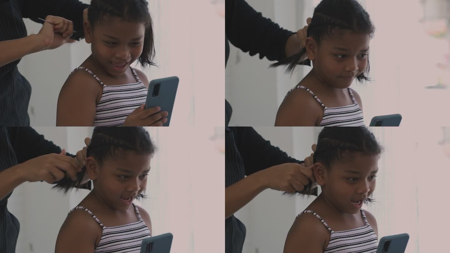 给女儿做发型。黑人小女孩扎辫子看手机