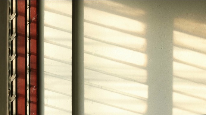 时间流逝：阳光透过百叶窗照射到白色的混凝土墙上。