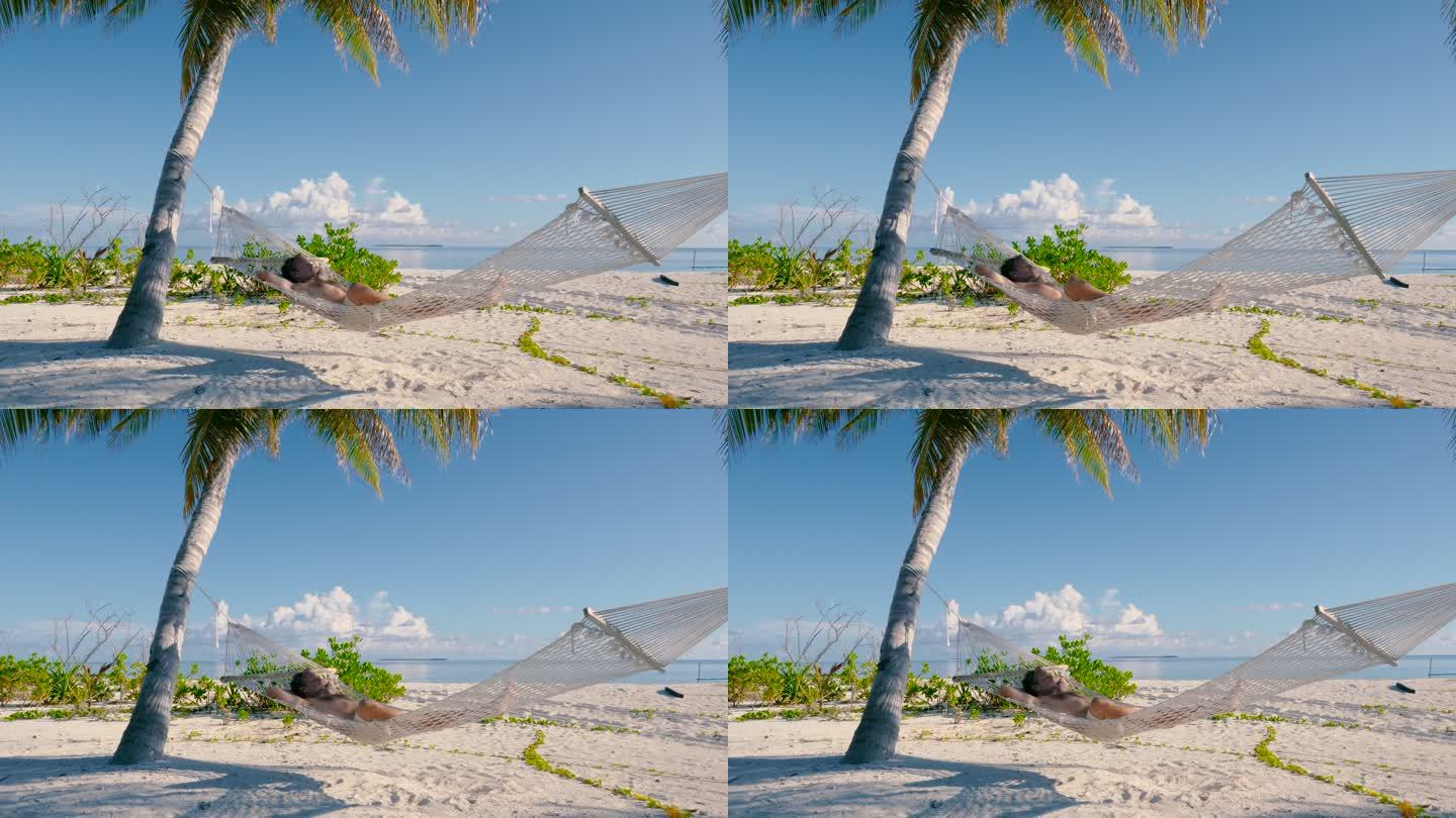 一名男子躺在海滩上两棵棕榈树之间的吊床上