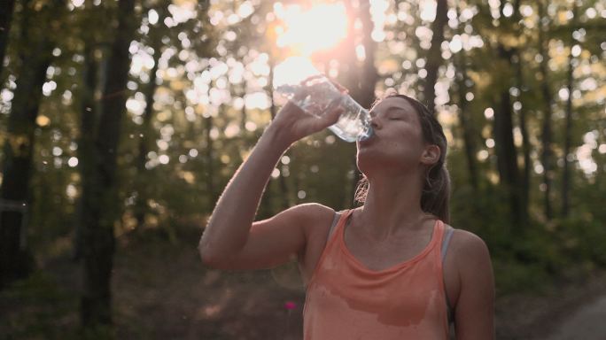 疲惫的女运动员在大自然中饮用淡水