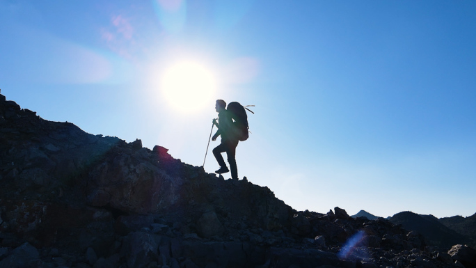 男人背着登山包登山逆光剪影攀登顶峰挑战