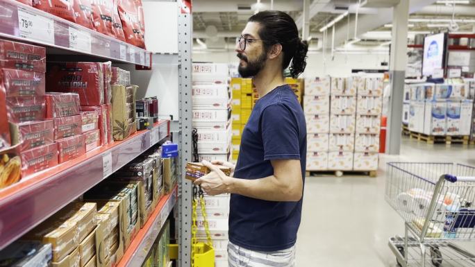 留胡子的男人在超市货架上挑选产品