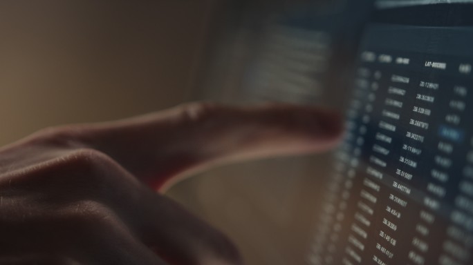 一名男子用手指在一台装有成排数据的电脑显示器上移动