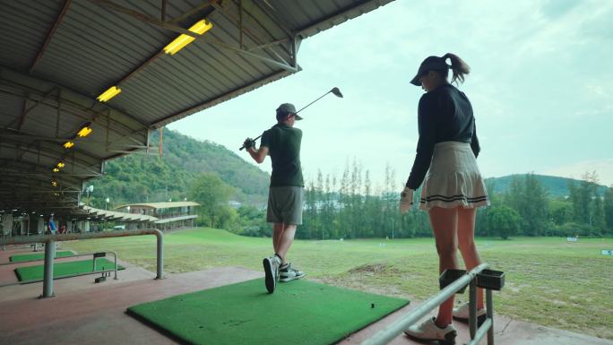 亚洲年轻女子高尔夫球手，在高尔夫练习场教年轻人打高尔夫。