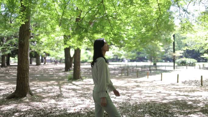 日本女人在公园里散步，在新鲜的绿叶下