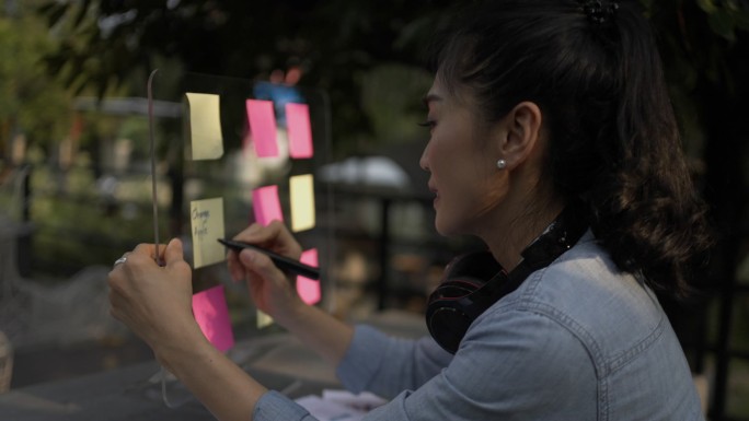 亚洲女人在贴在玻璃墙上的贴纸上写下想法。